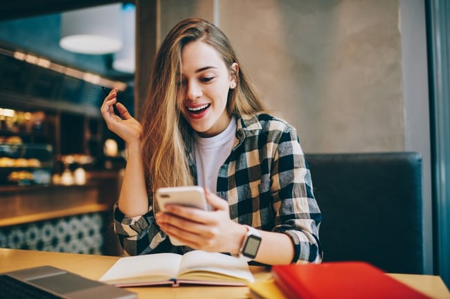 student looking at her phone happily surprised